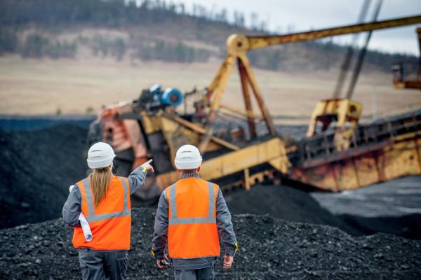 Coal Mine Workers Discussing With Each Other While Pointing Out An Excavator In Mining Field.